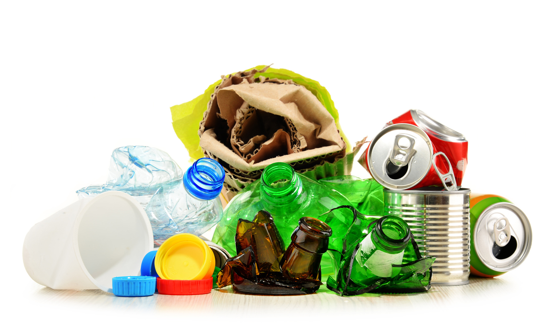 zdjęcie przedstawia zebrane w jednym miejscu na białym tle odpady plastikowe, papierowe  i metalowe butelki, kartony  i puszki