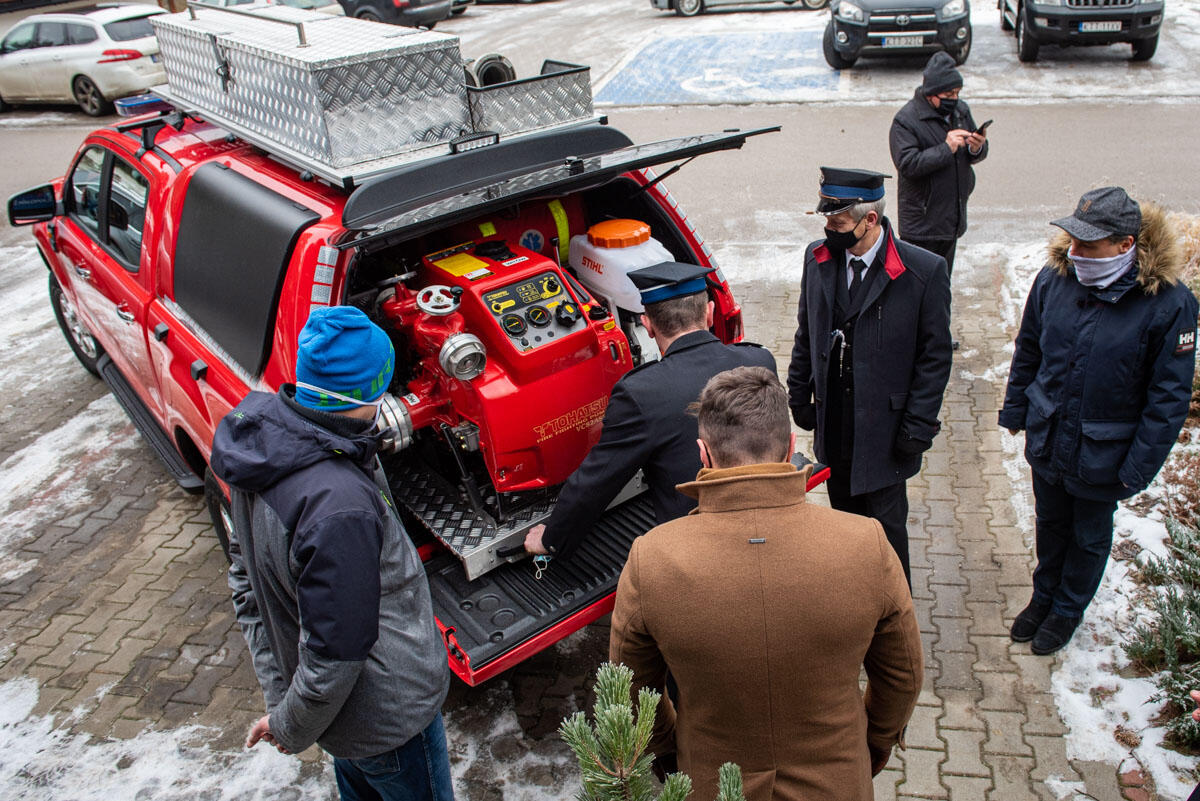 Zdjęcie pokazuje kilka osób w tym dwie w galowych mundurach strażackich oglądających pompę wodną w bagażniku samochodu strażackiego typu pickup